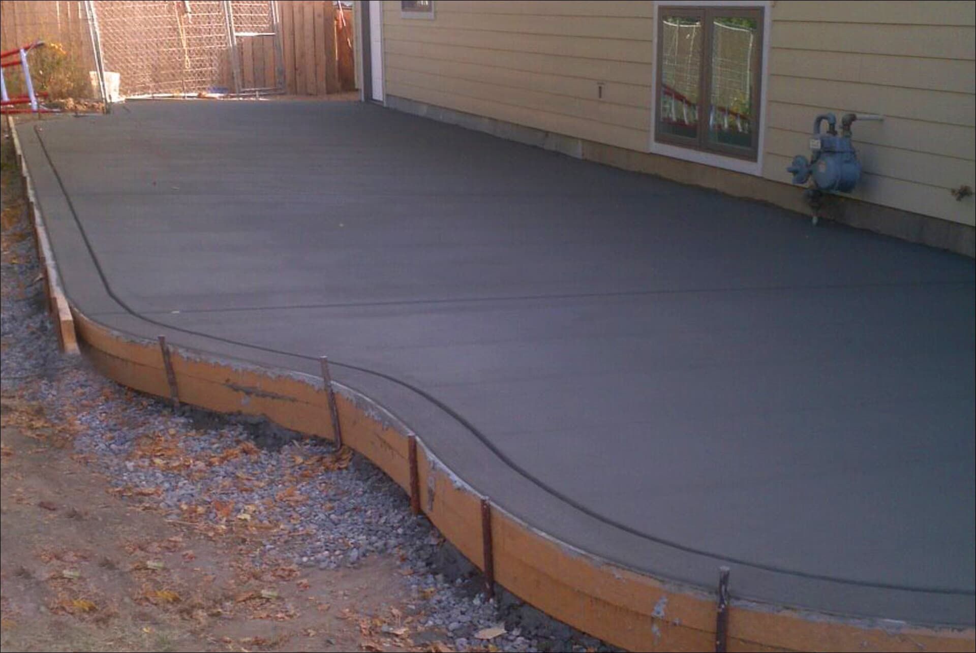 Newly poured concrete patio, curved edge, next to a beige house wall.