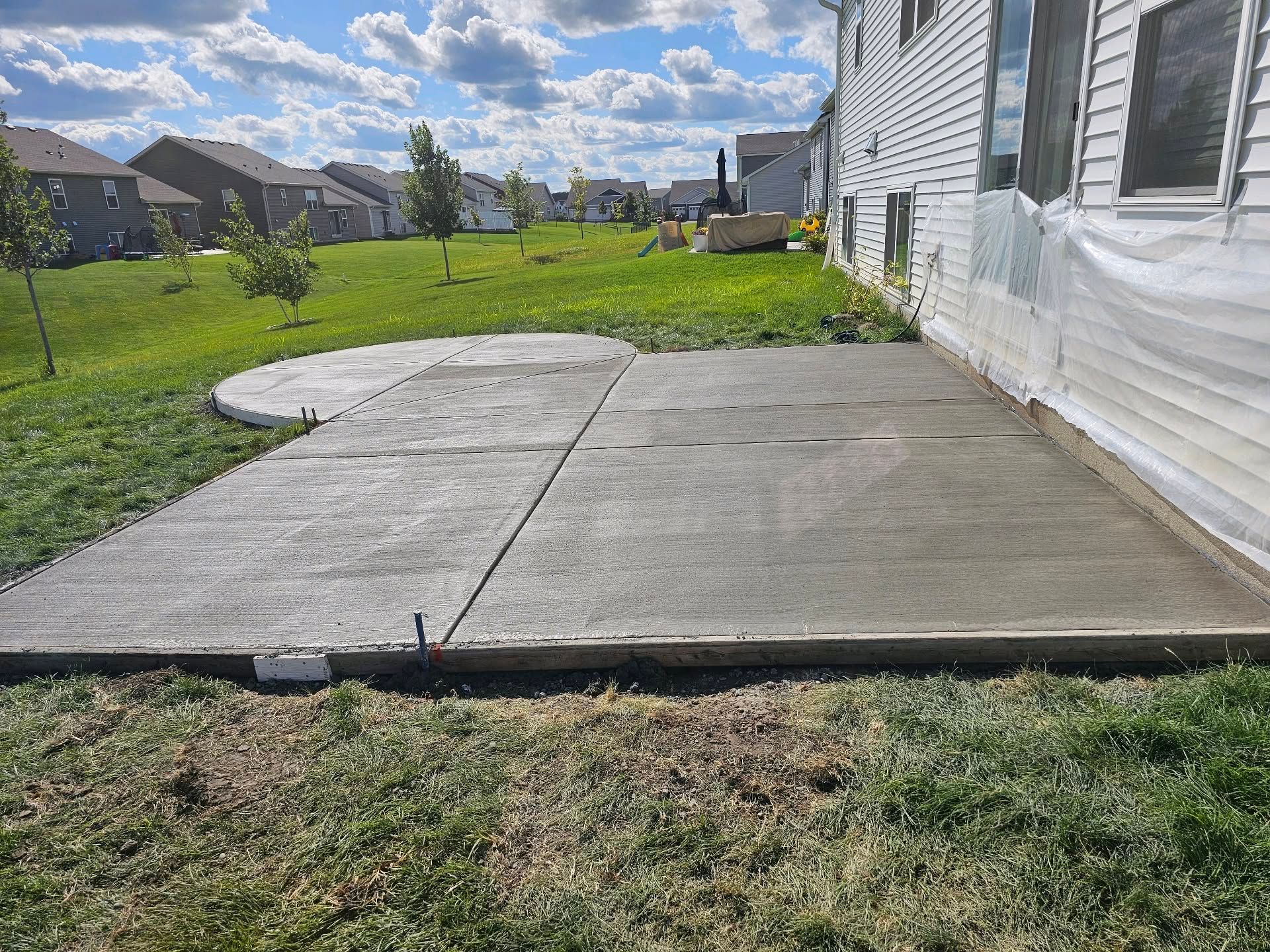 Newly poured concrete patio in a backyard with grass and houses in the background.