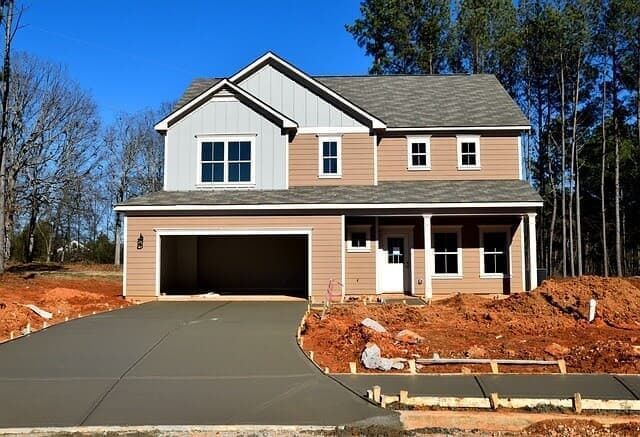 New construction two-story house with a newly poured concrete driveway and red dirt landscaping.