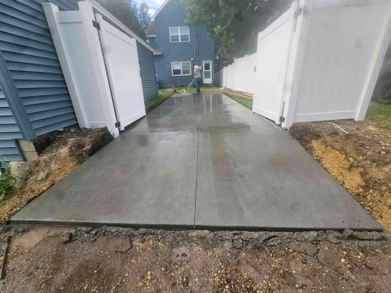 Freshly poured concrete patio between white fences and a blue house.