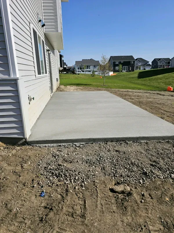 New concrete patio adjacent to a house with white siding on a sunny day.