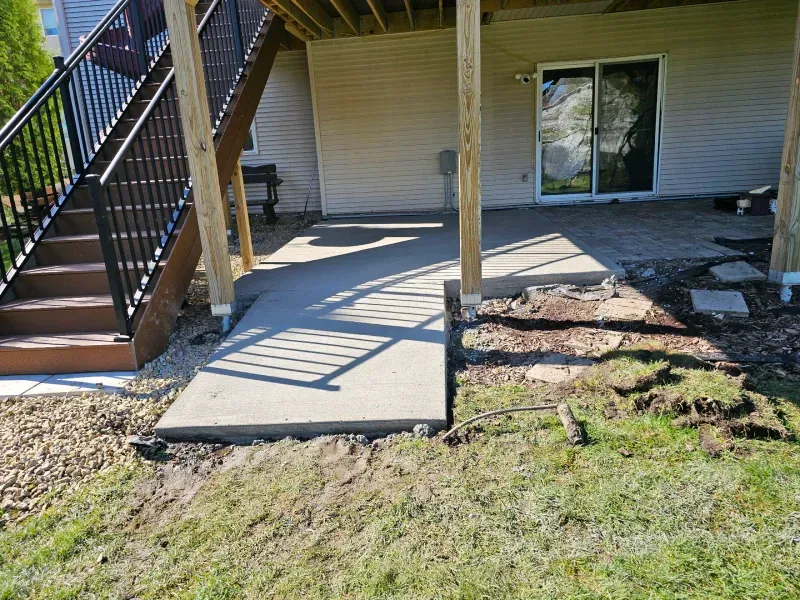 Concrete patio with a pathway and wooden support beams beneath a deck.