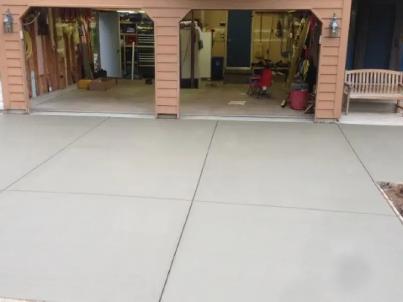 Newly poured concrete driveway leading to a two-car garage. Brown garage frame and a bench are visible.