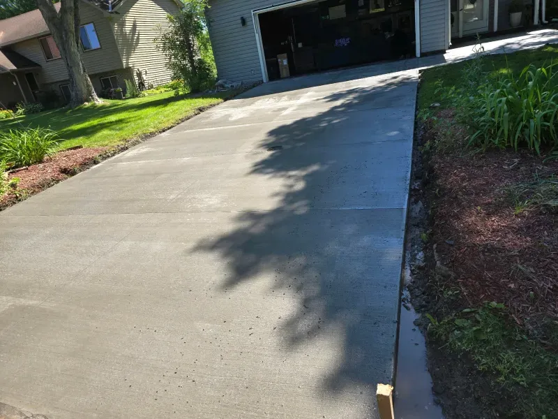 Newly poured concrete driveway with a garage in the background, surrounded by grass and landscaping.