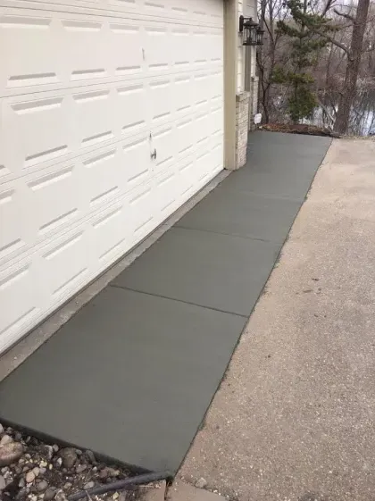 Freshly poured concrete walkway alongside a garage door.