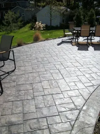 Gray stamped concrete patio with outdoor furniture and a green lawn in the background.