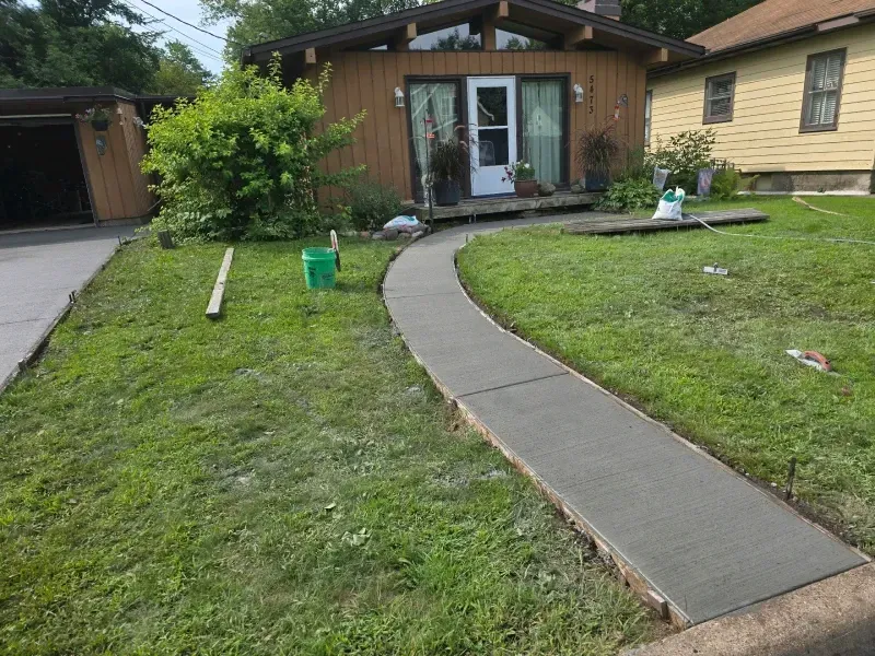 New concrete walkway leading from a driveway to the front door of a brown house.