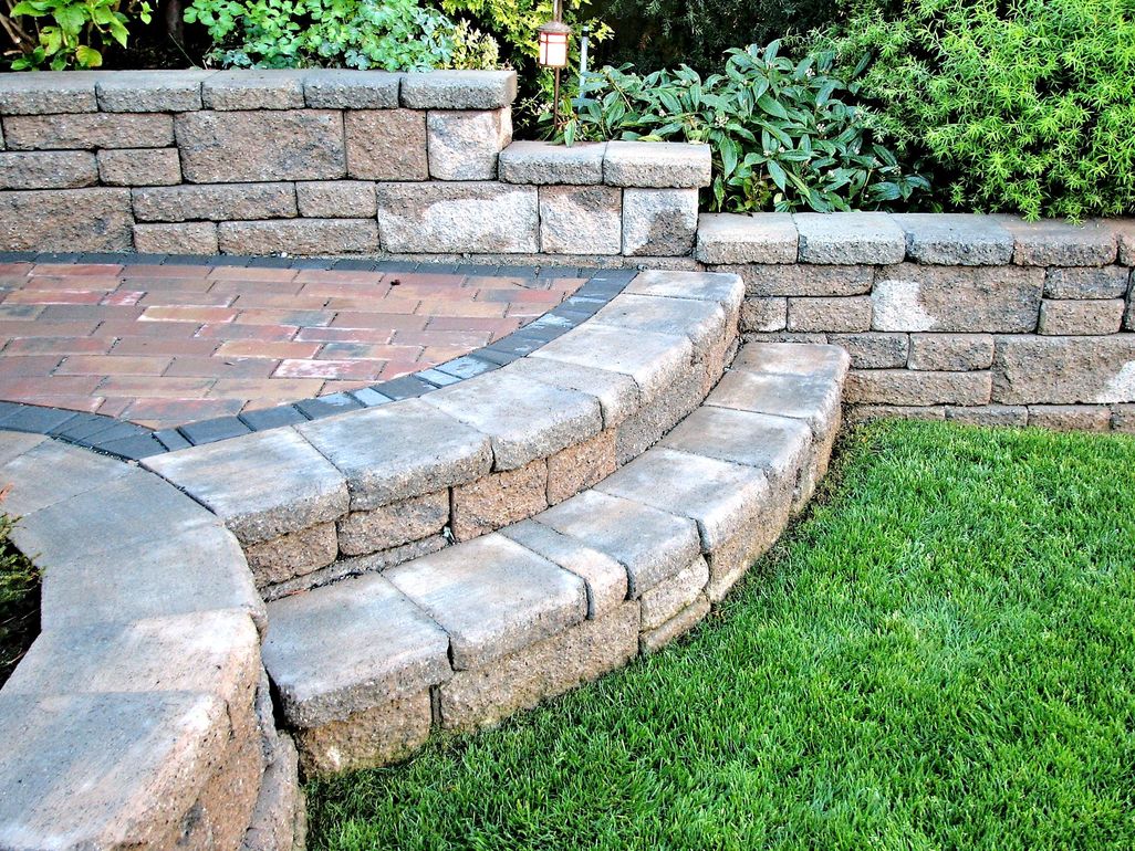 Stone steps and retaining walls with brick patio and green lawn.