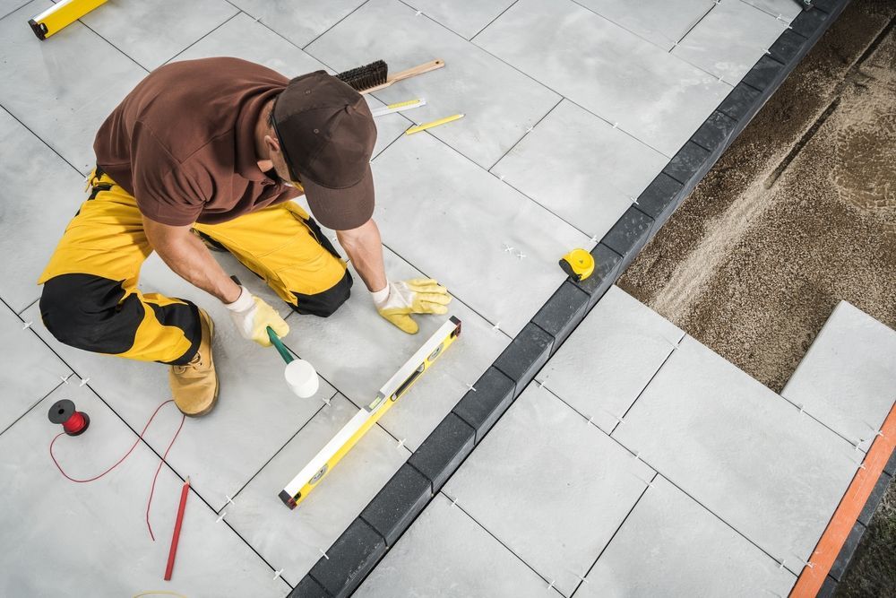 Construction worker laying gray paving stones, using level and rubber mallet. Outdoors.