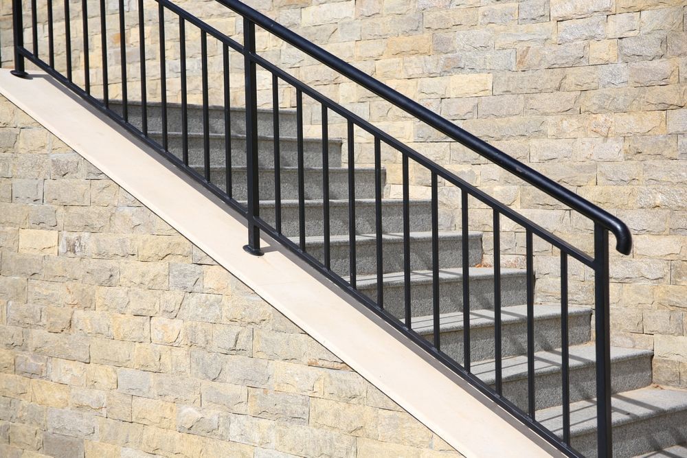 Black metal handrail on outdoor stairs with stone wall background.