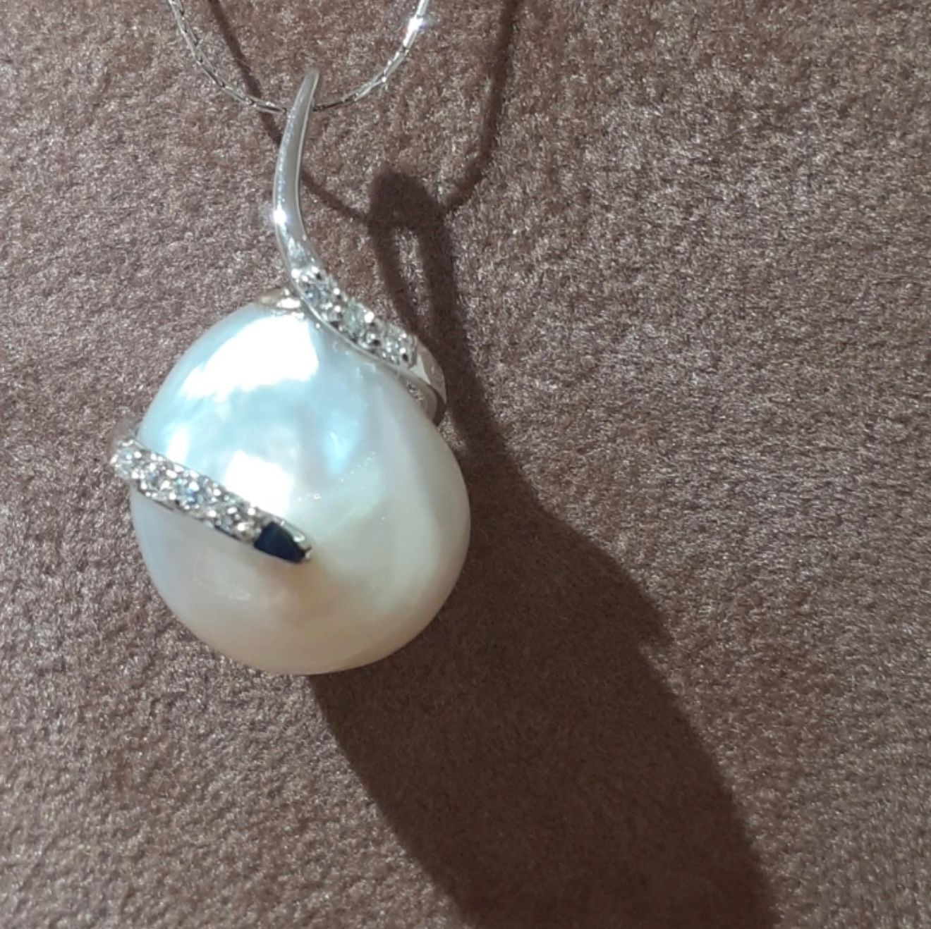 Ciondolo di perla con motivo a spirale argentato simile a un diamante su sfondo di tessuto marrone.