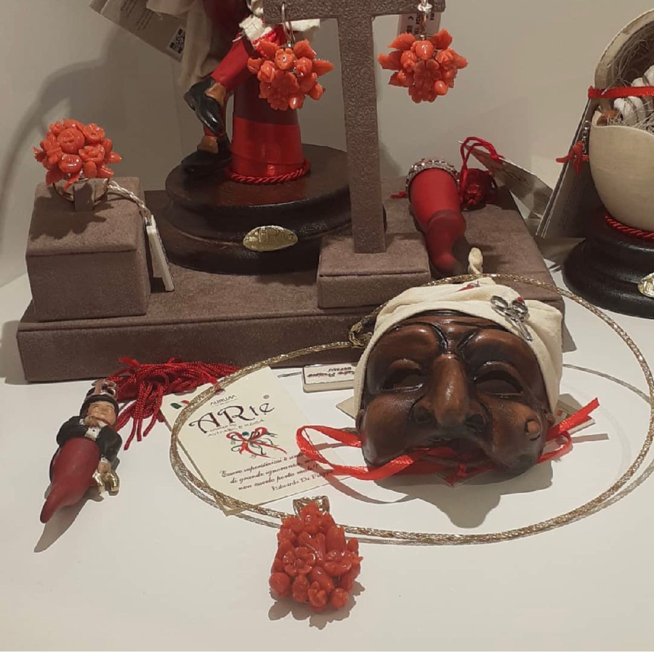 Composizione artistica di maschere intagliate e decorazioni floreali rosse su una superficie bianca.