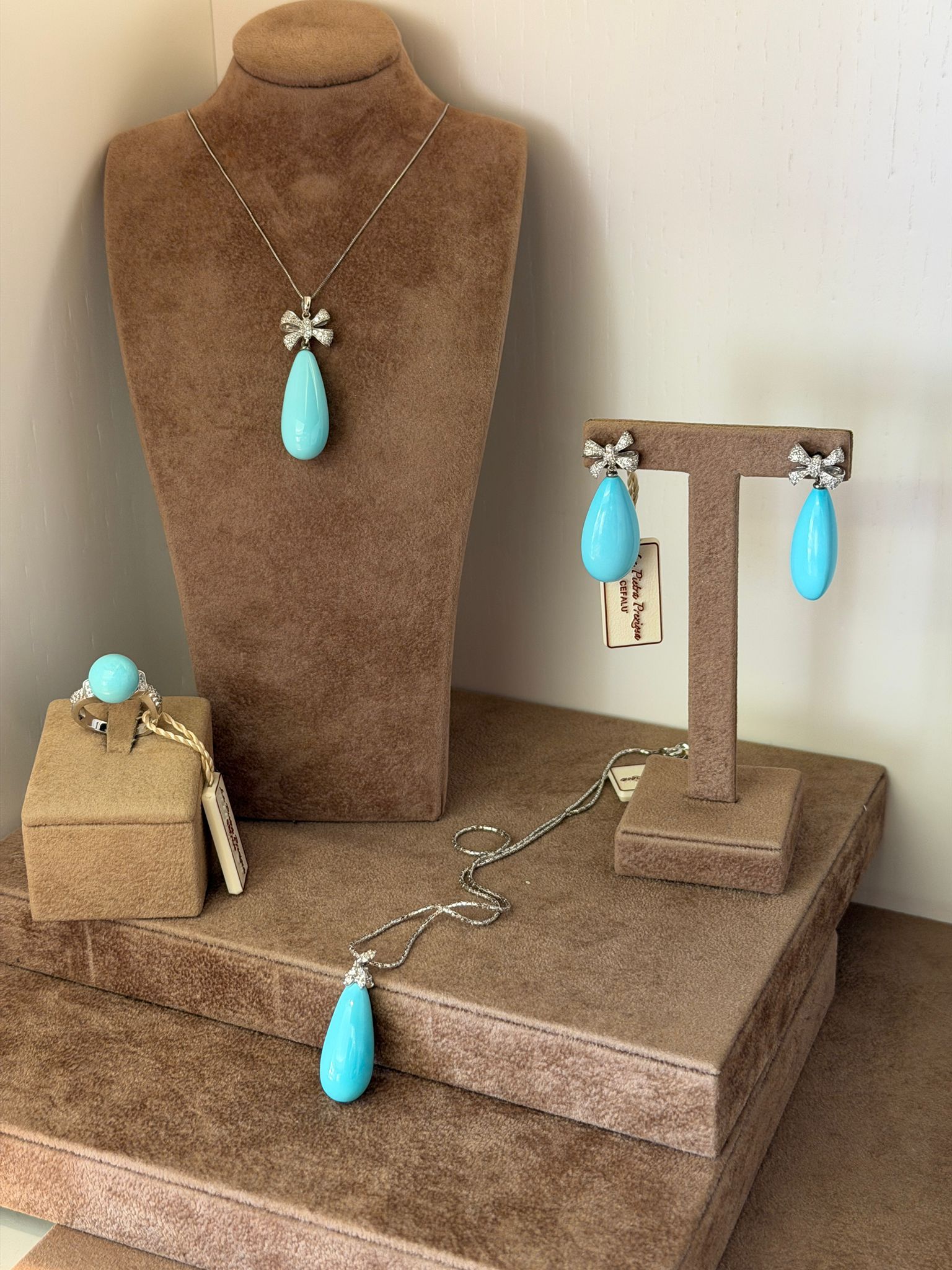 Espositore per gioielli marrone con collana con pendente turchese, orecchini, bracciale e anello su supporti e scatola.