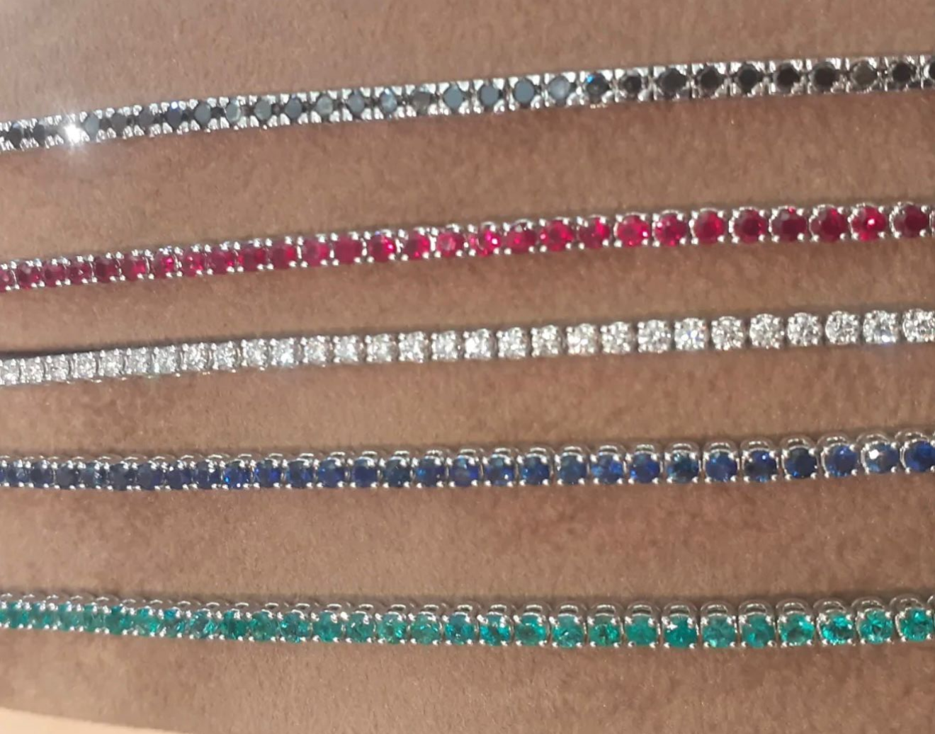 Quattro braccialetti scintillanti di perline rosse, argento, blu e turchesi disposti orizzontalmente su una superficie marrone.