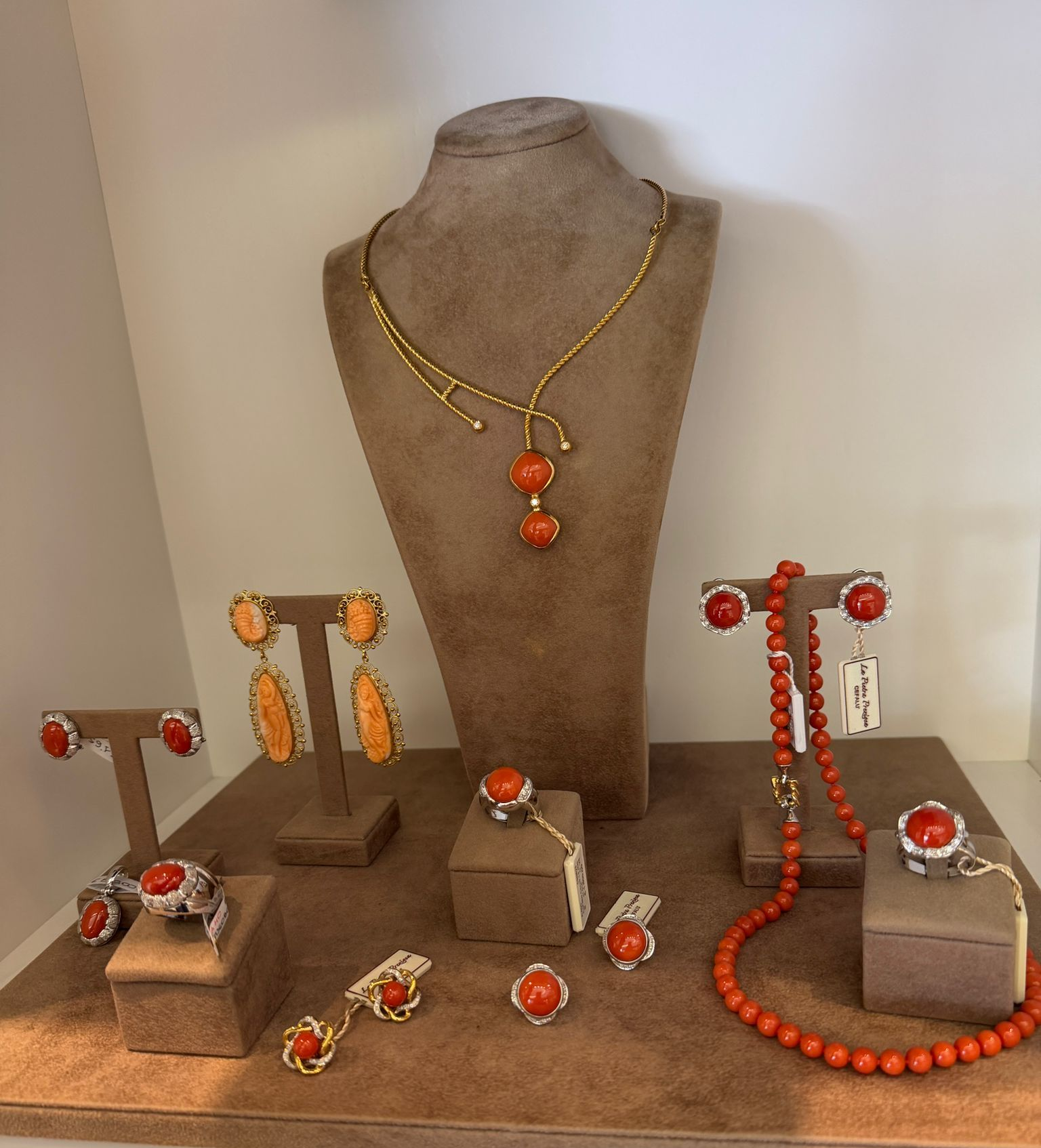Gioielli in oro e corallo esposti su supporti e blocchi di velluto su uno sfondo neutro.