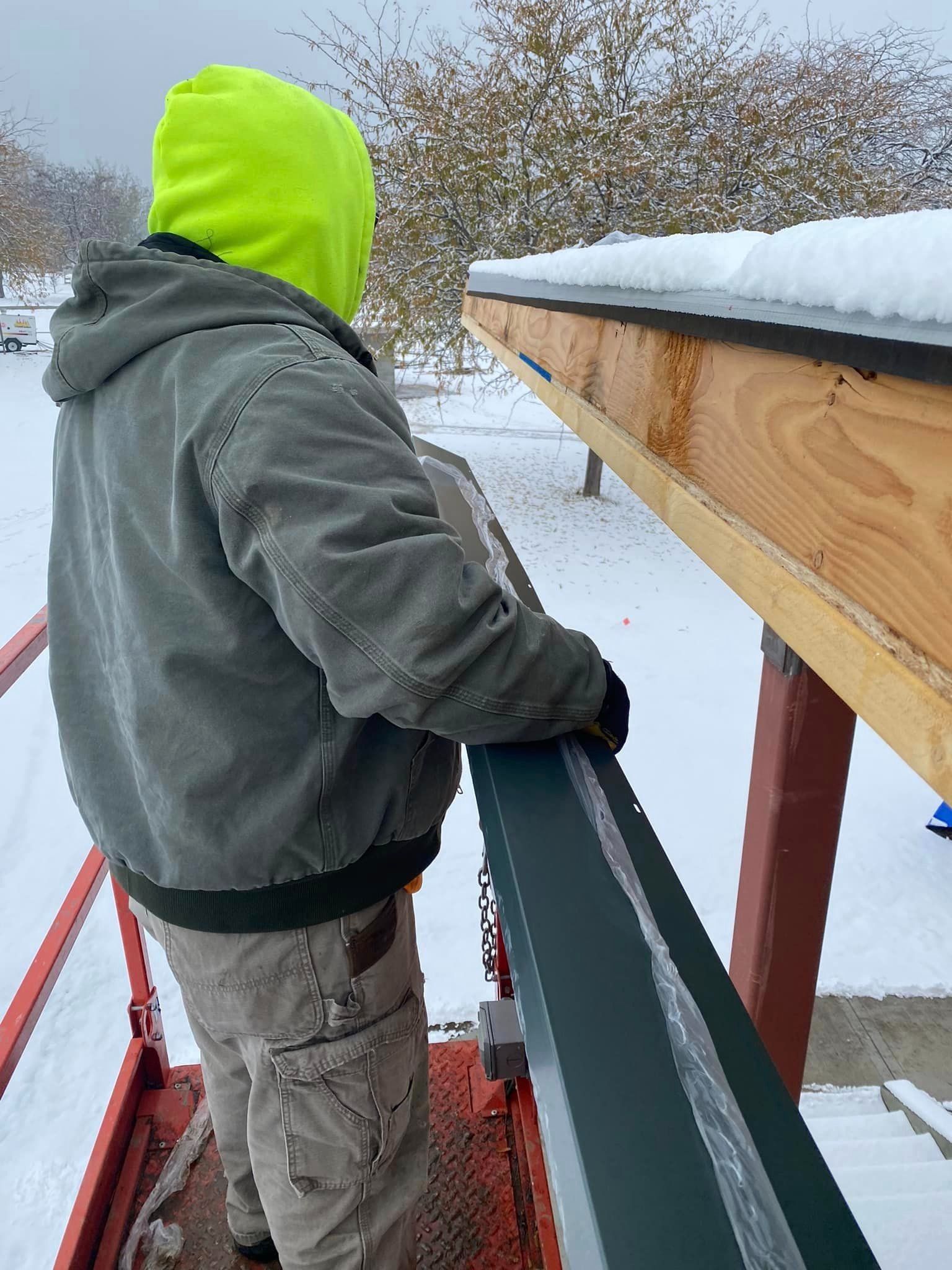A man wearing a neon yellow hoodie is standing on a ladder in the snow.