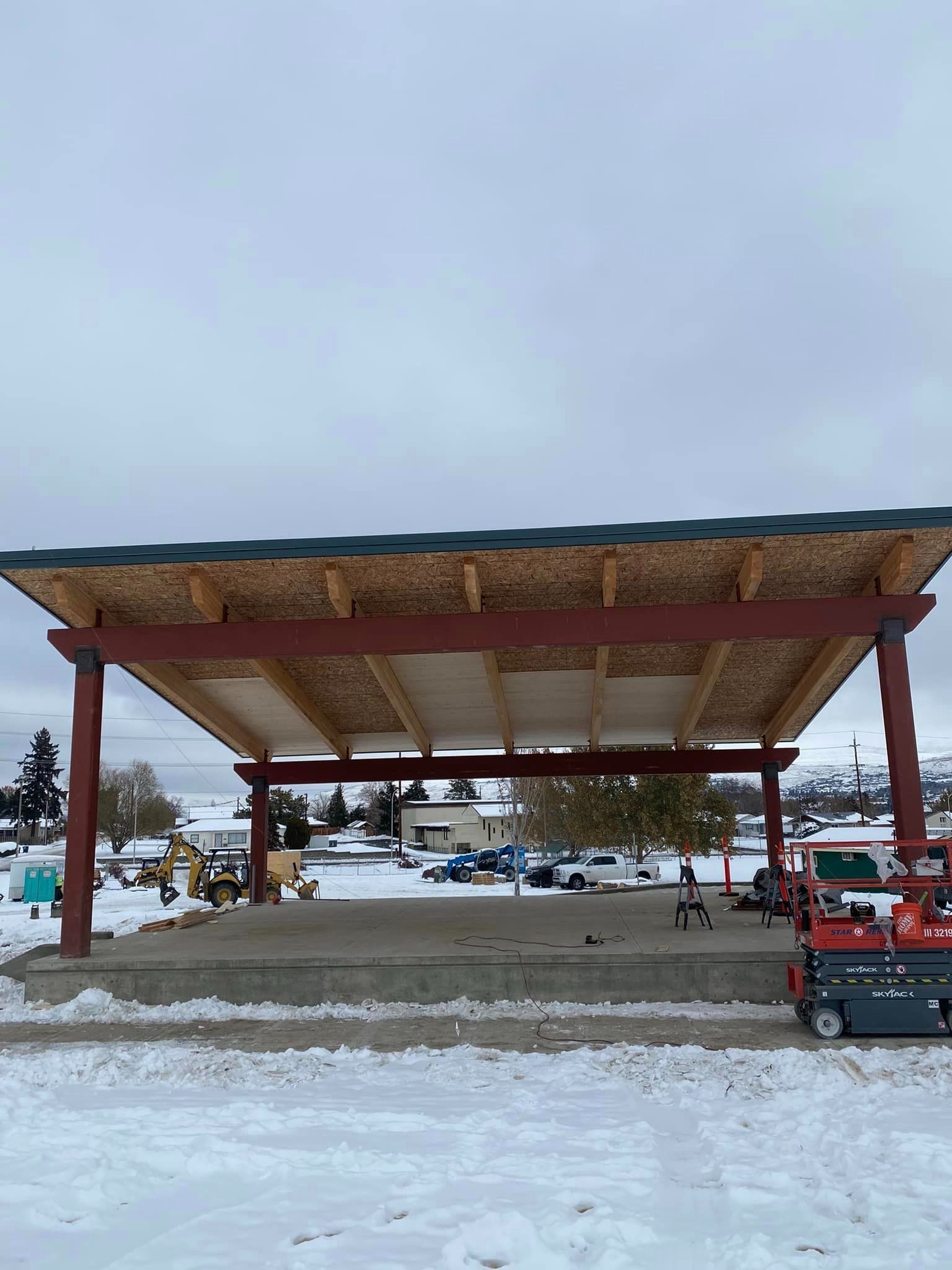 A snow blower is parked under a wooden structure in the snow.
