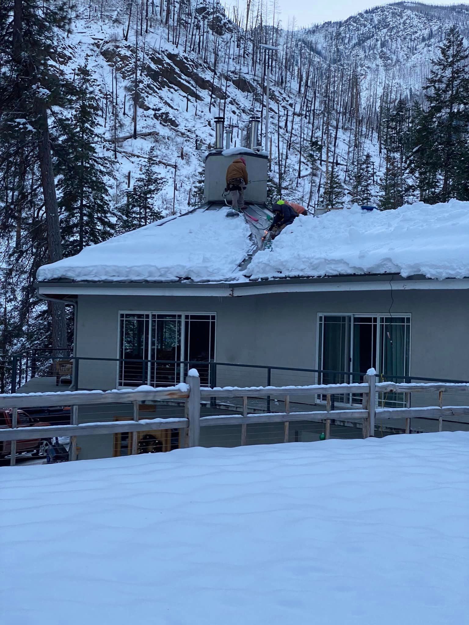 A person is standing on the roof of a house covered in snow.