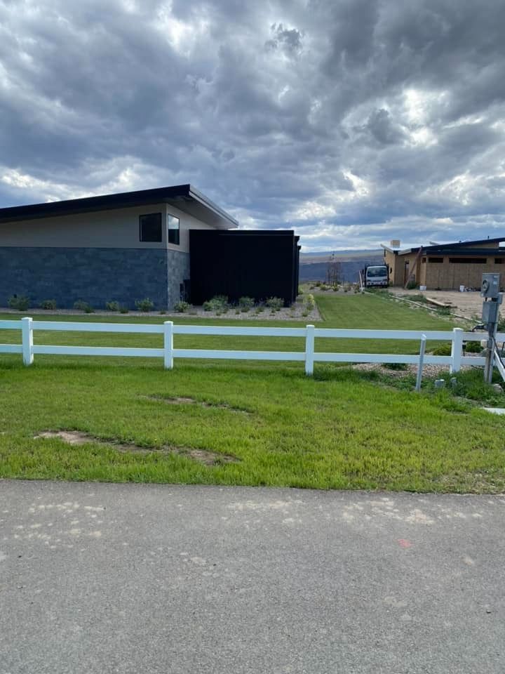A white fence surrounds a lush green field in front of a house.