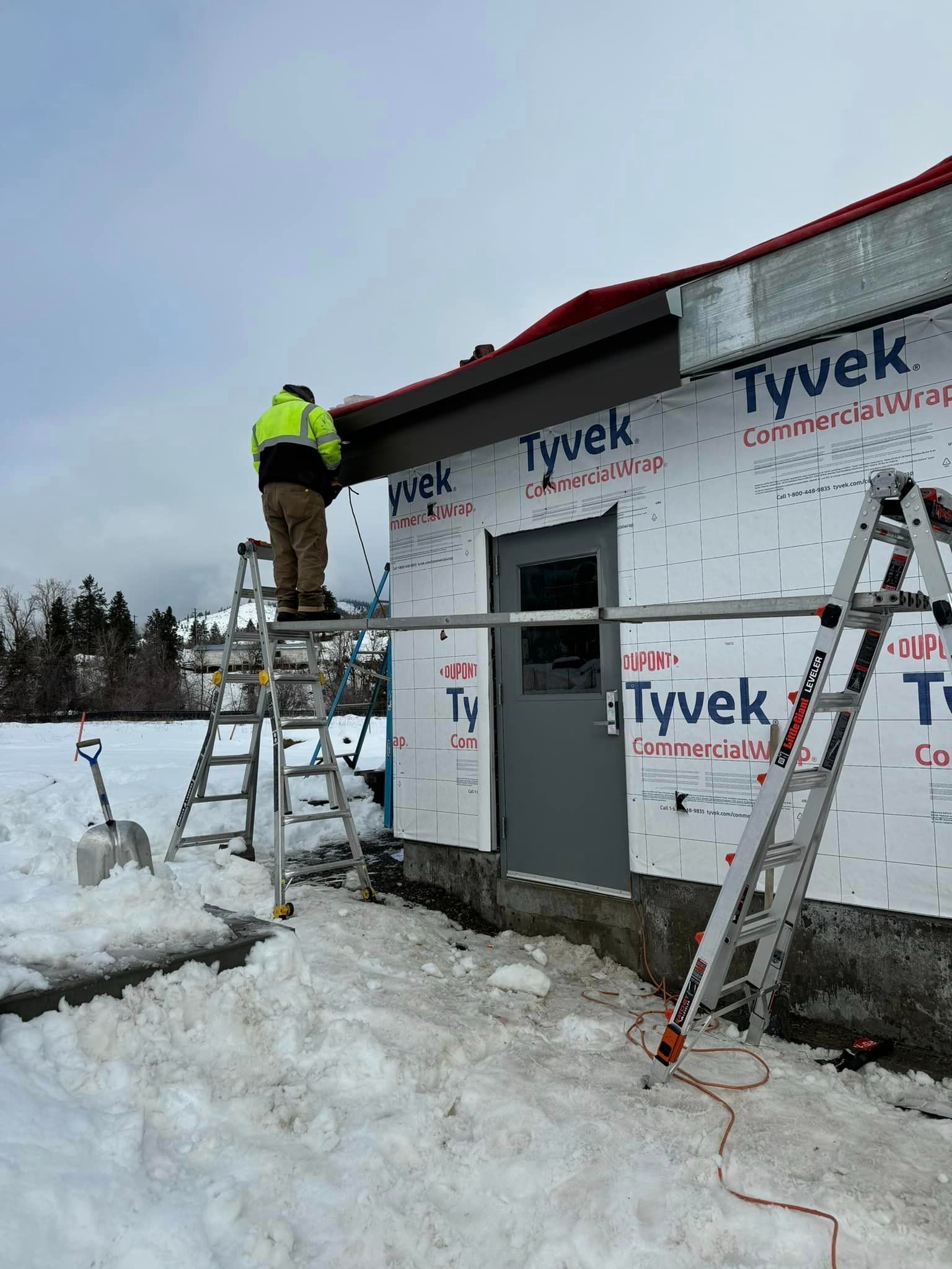 A man is standing on a ladder in front of a building in the snow.