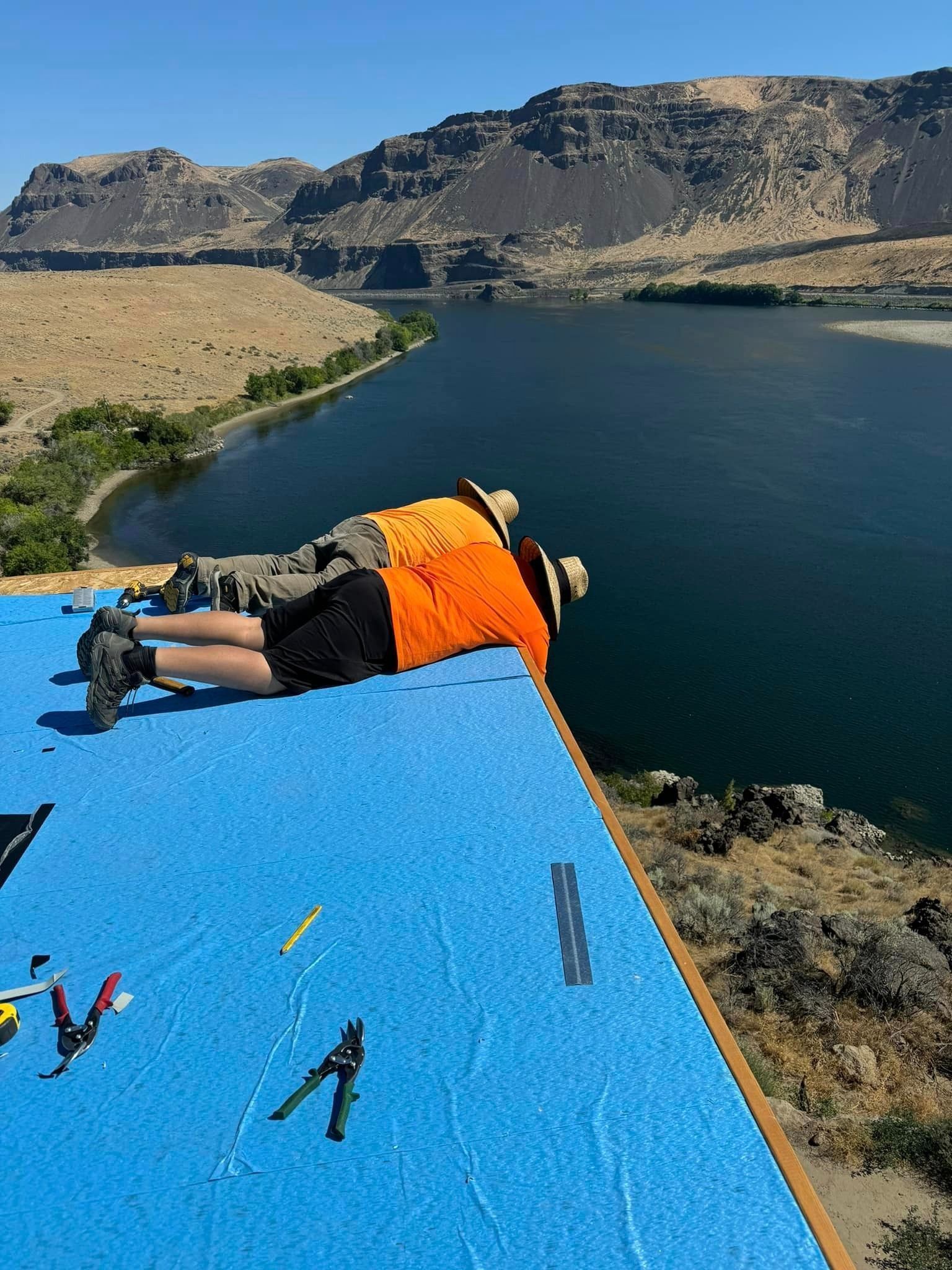 A man is laying on a blue roof overlooking a lake.