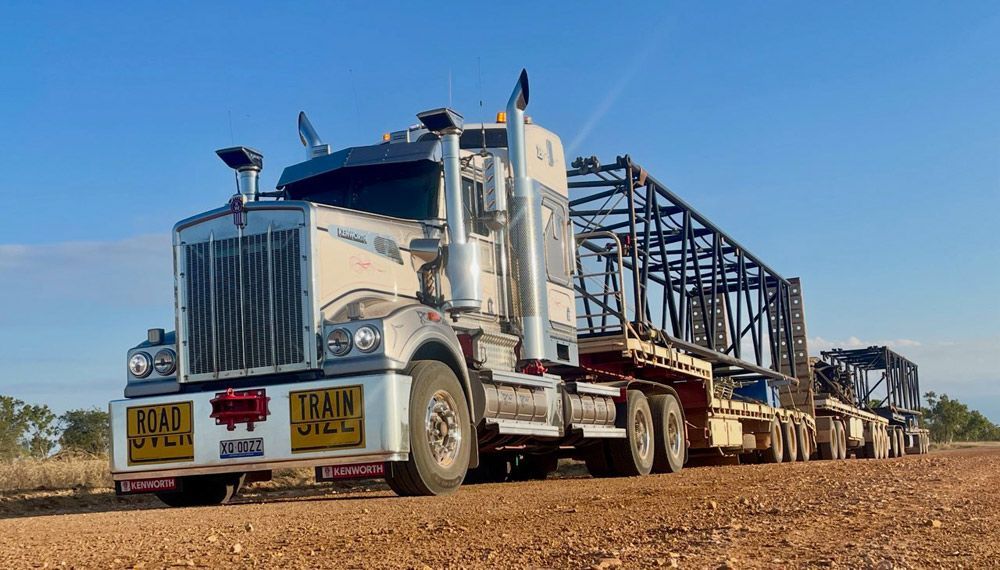 White Semi-truck With Oversized Load Driving On A Dirt Road — ECC Heavy Haulage in Ormeau, QLD