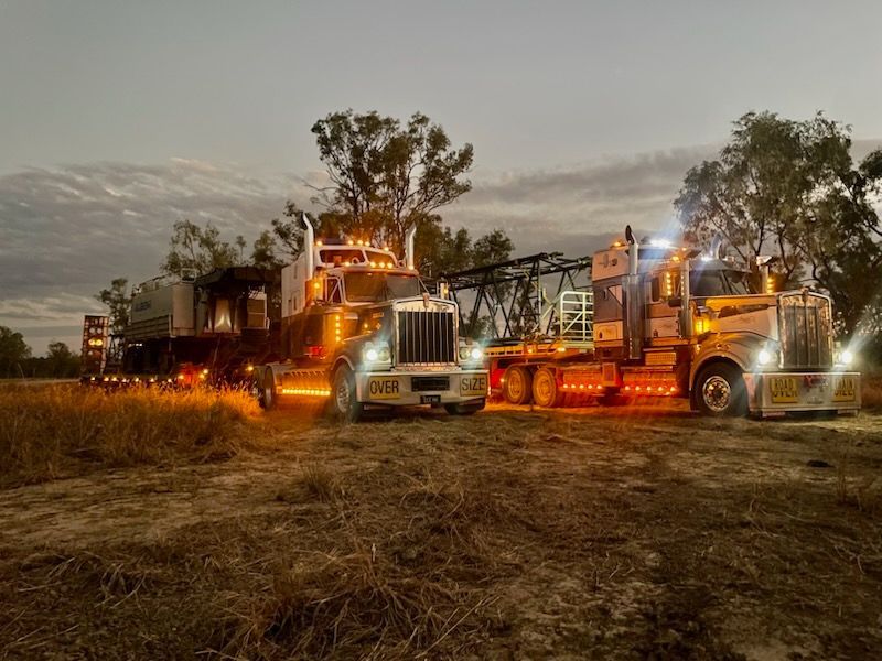 Two Semi-trucks With Trailers Parked at Dusk; Lit Headlights and Amber Lights, Outdoors — ECC Heavy Haulage in Gold Coast, QLD
