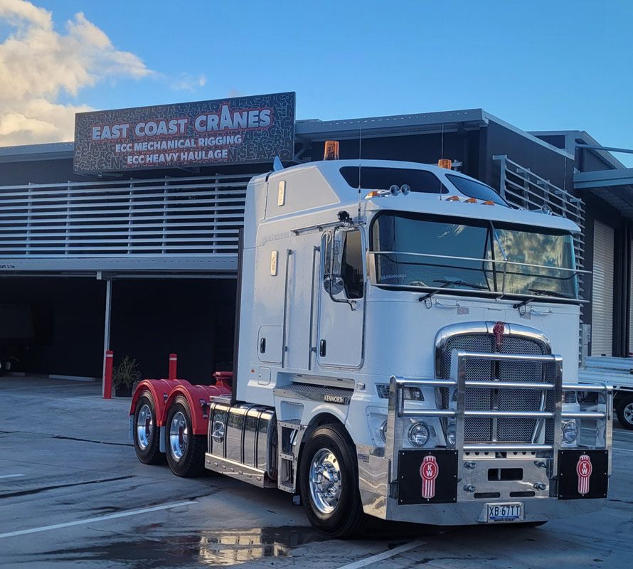 White Kenworth truck parked in front of East Coast Cranes building; red accents, blue sky. — ECC Heavy Haulage in Ormeau, QLD
