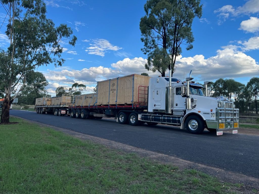 White Semi-truck Hauling Multiple Flatbed Trailers Loaded With Large Wooden Crates on a Road Under a Cloudy Sky — ECC Heavy Haulage in Gold Coast, QLD