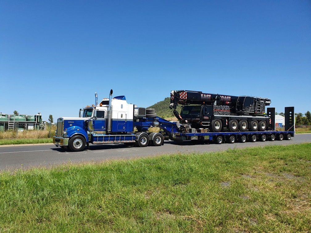 Blue and white semi-truck hauling a large black machine on a multi-axle trailer — ECC Heavy Haulage in Ormeau, QLD