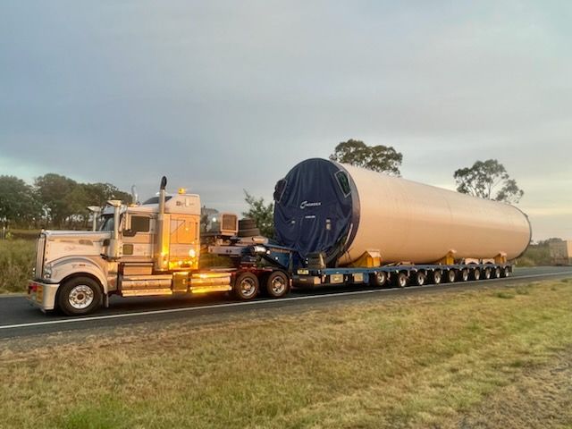 Truck hauling a large, cylindrical wind turbine component on a highway in a rural setting — ECC Heavy Haulage in Ormeau, QLD