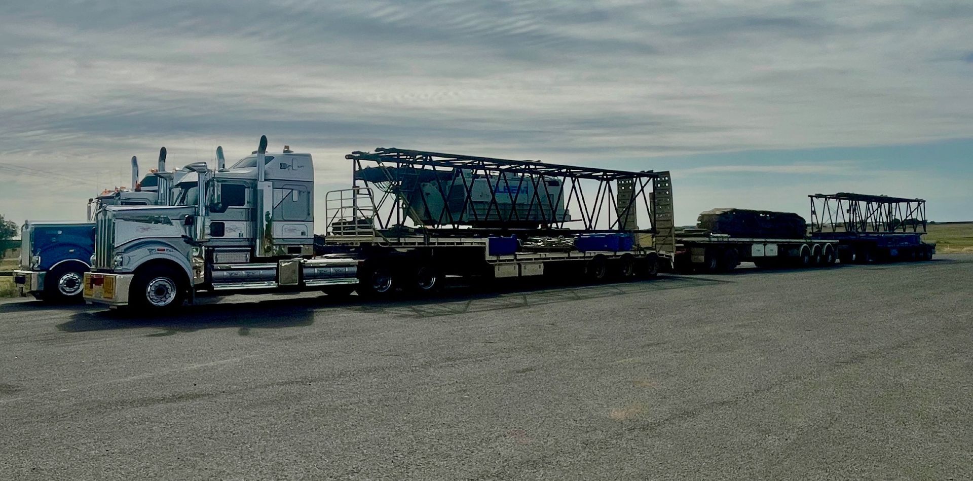 Three semi-trucks parked on a gravel lot, hauling large metal framed cargo — ECC Heavy Haulage in Ormeau, QLD