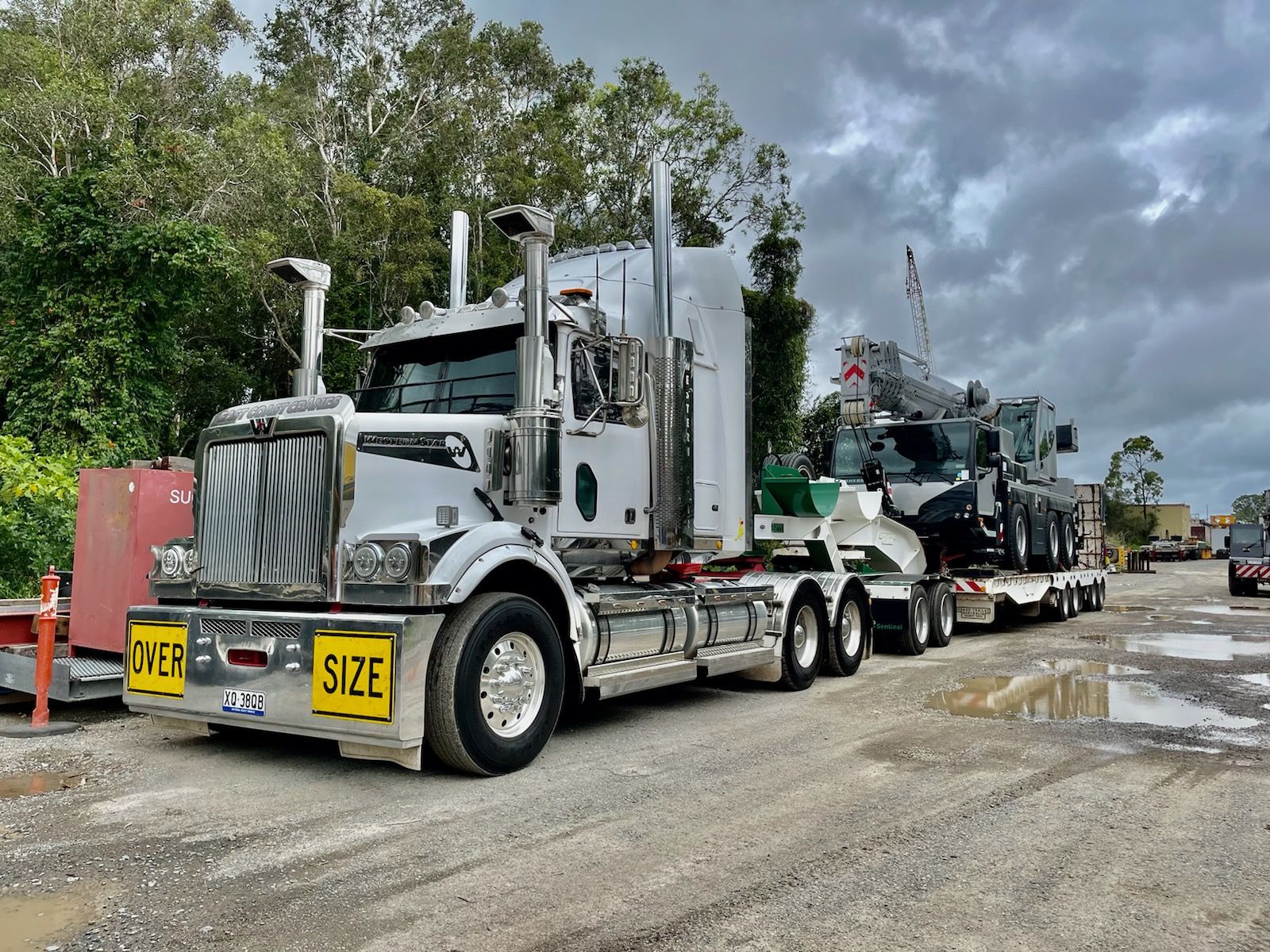 White Semi-truck Transporting a Crane on a Flatbed Trailer on a Muddy Road — ECC Heavy Haulage in Gold Coast, QLD