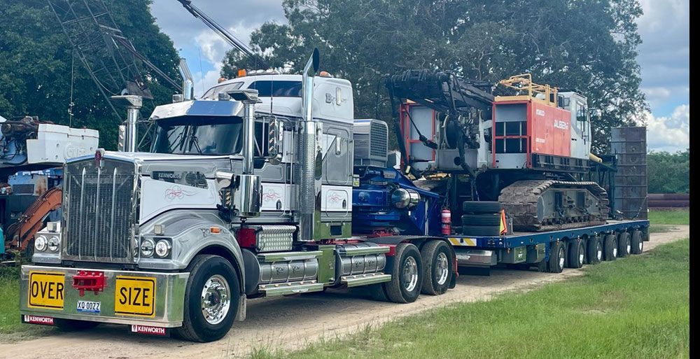 Large Silver Semi-truck Hauling Oversized Excavator on a Lowboy Trailer — ECC Heavy Haulage in Ormeau, QLD