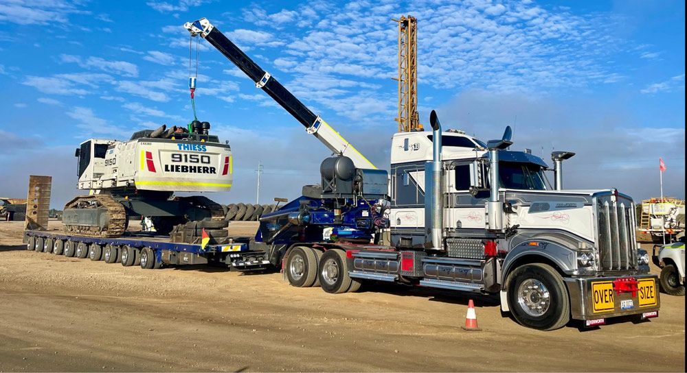 A Large Truck Transports Heavy Machinery On A Flatbed — ECC Heavy Haulage in Brisbane, QLD