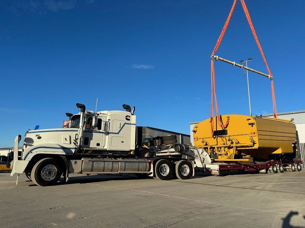 White Semi-truck Transports Yellow Equipment Under A Crane — ECC Heavy Haulage in Brisbane, QLD