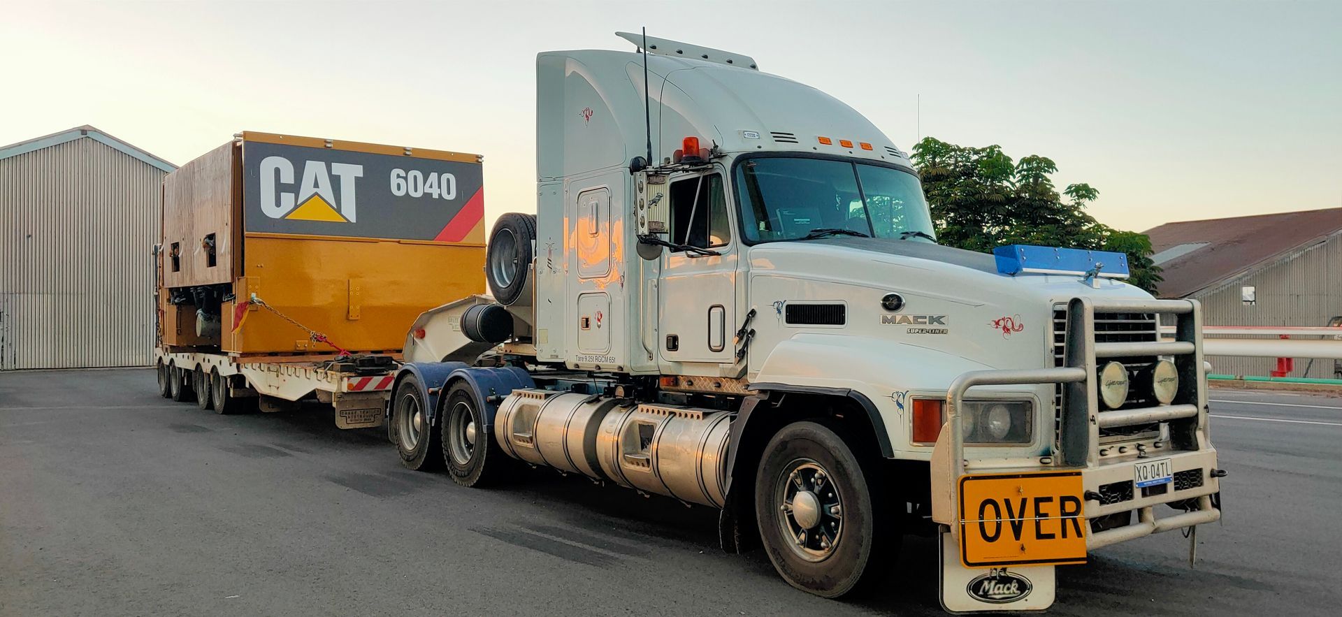 White semi-truck hauling a large yellow CAT machine — ECC Heavy Haulage in Ormeau, QLD