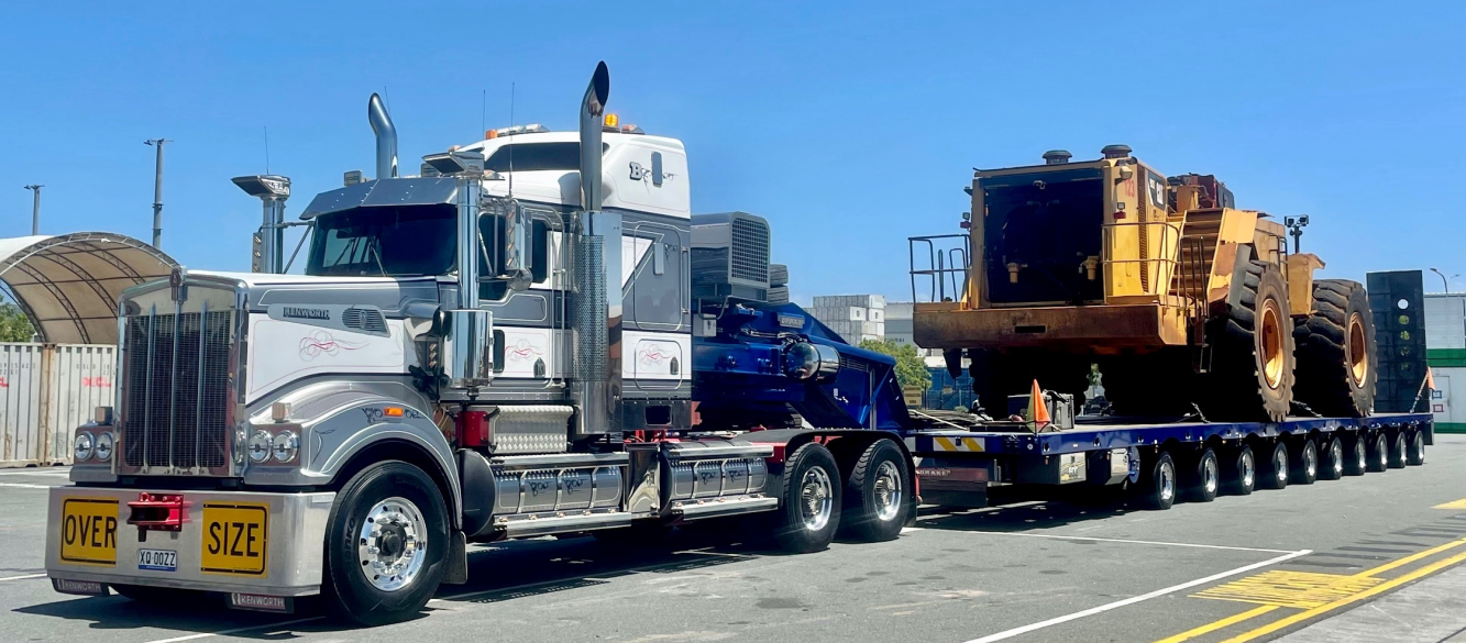 Semi-truck transporting oversized construction equipment on a sunny day — ECC Heavy Haulage in Ormeau, QLD