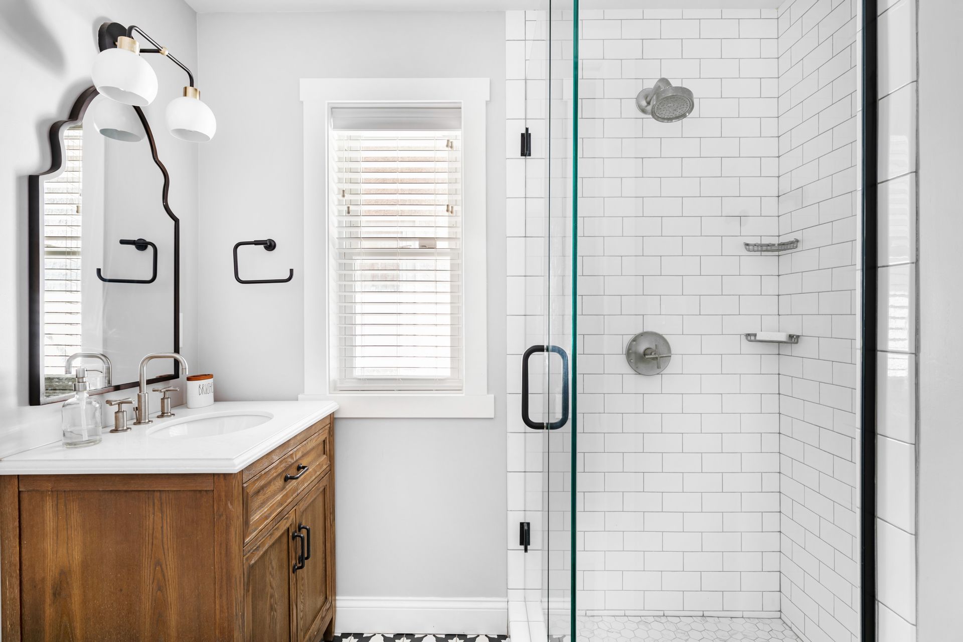 Bathroom with wood vanity, white subway tile shower, and window with blinds.