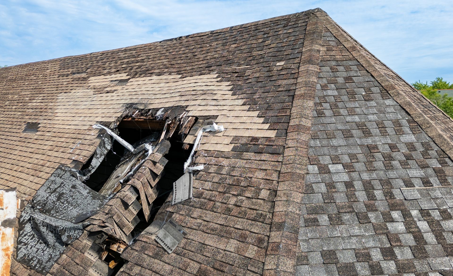 Damaged roof with a large collapsed hole exposing broken wooden beams and shingles