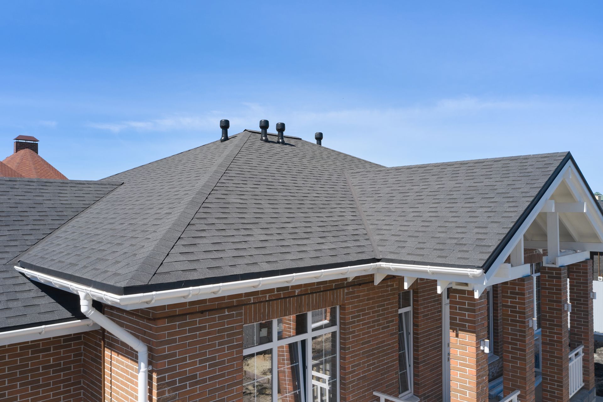 Brick building with a dark gray shingled roof, white trim, and a bright blue sky.