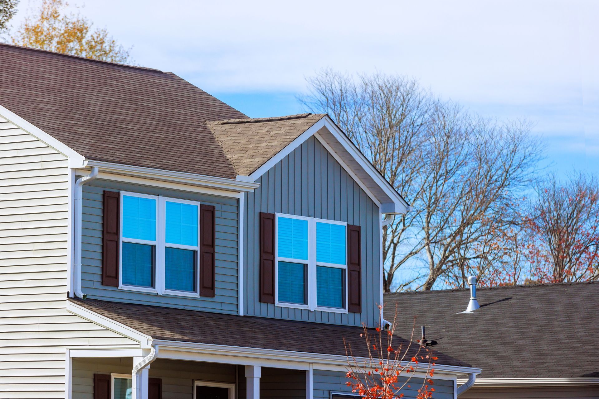Two-story house with gray siding and blue-tinted windows under a blue sky.