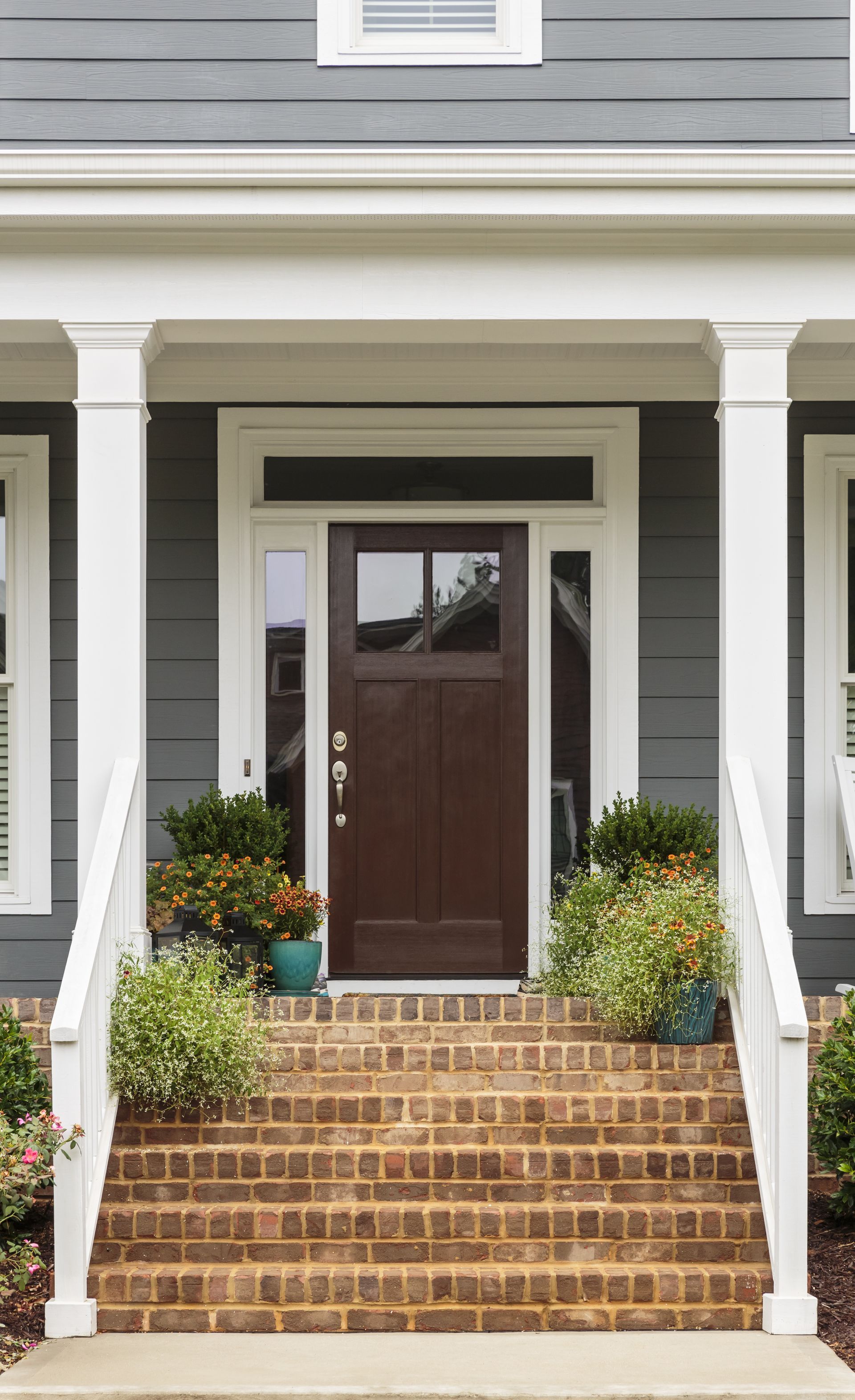 Brown front door with sidelights and steps leading up to a gray house with white columns.