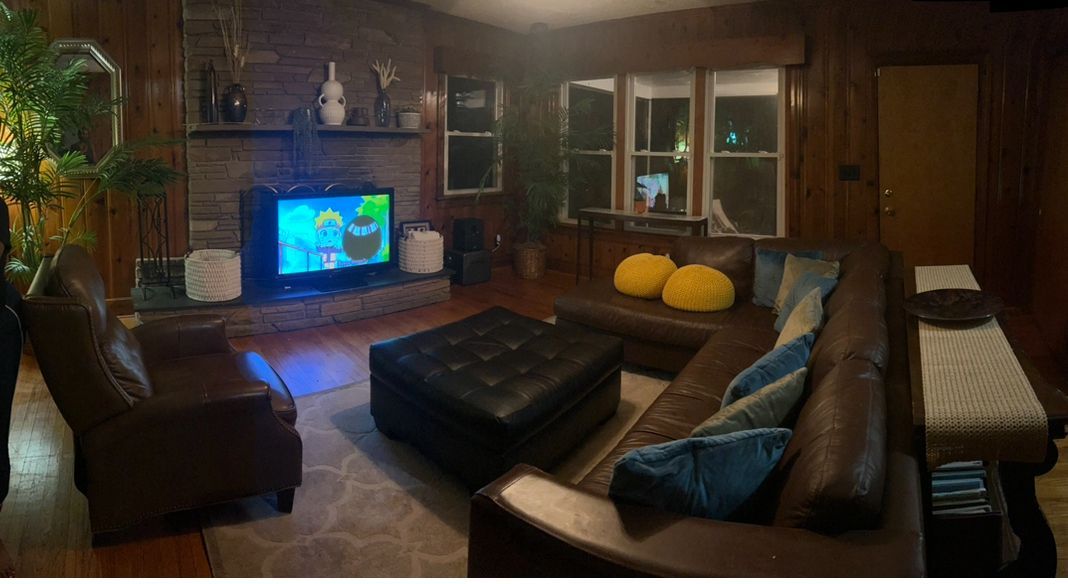 Living room with dark wood paneling, leather furniture, fireplace, and TV displaying a cartoon.