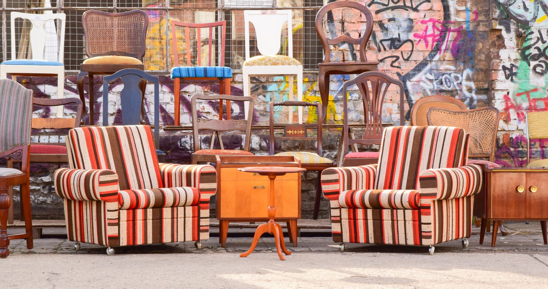 Two striped armchairs face a small table, with many stacked chairs and graffiti in the background.