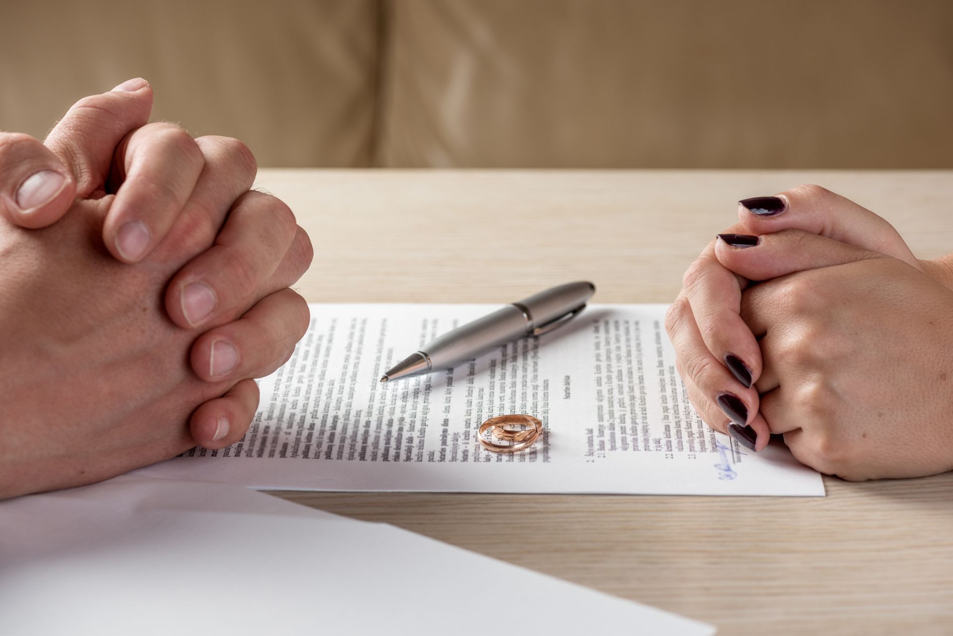 Hands clasped over divorce papers, wedding ring, pen on a table, signifying a legal separation.