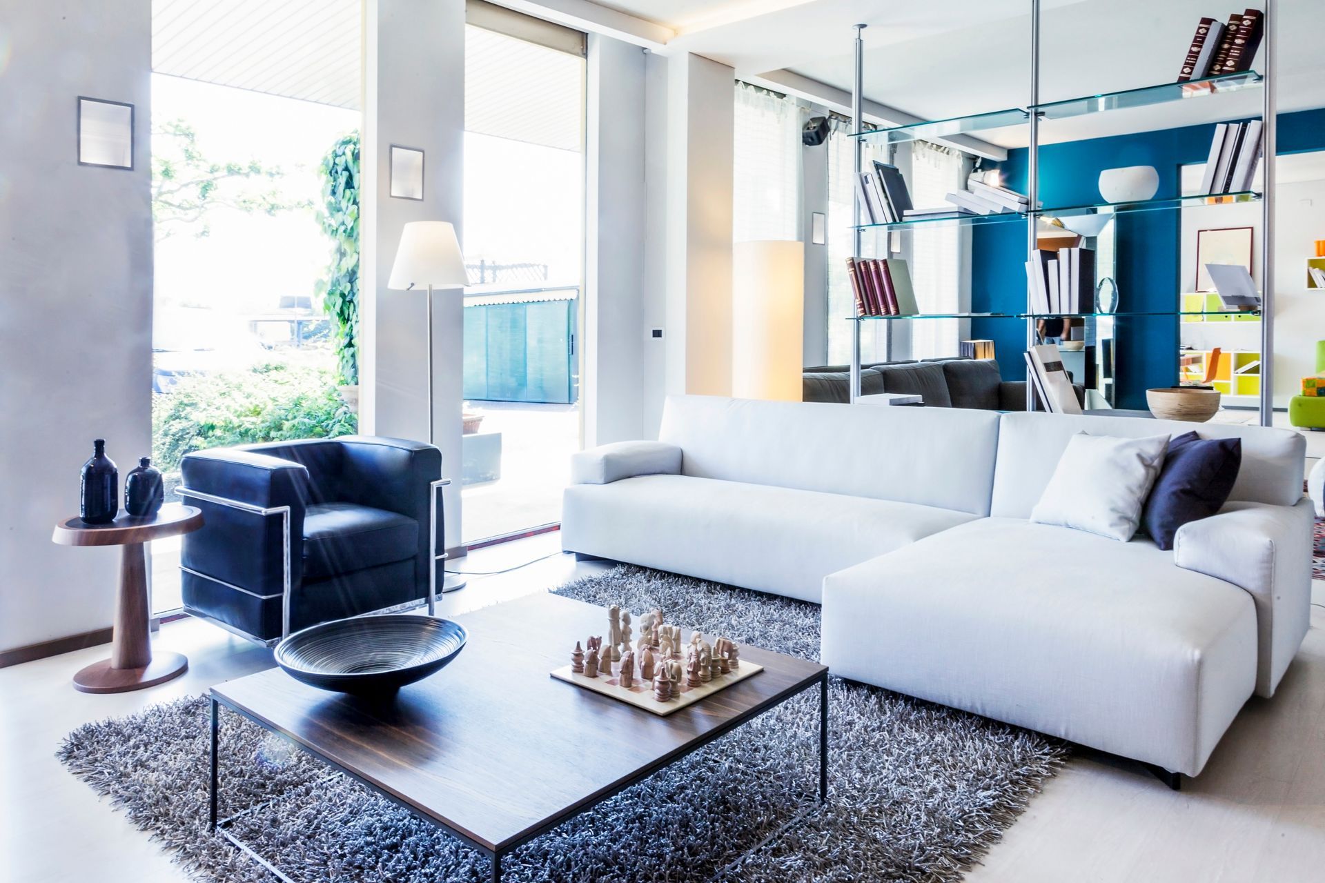Modern living room with white sectional sofa, blue armchair, and large windows.