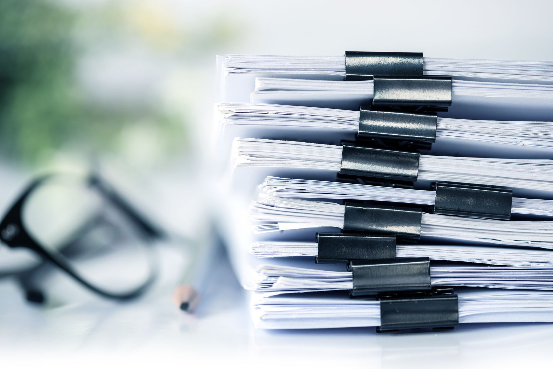 Stack of white papers held together with binder clips, with eyeglasses and a pencil in the background.