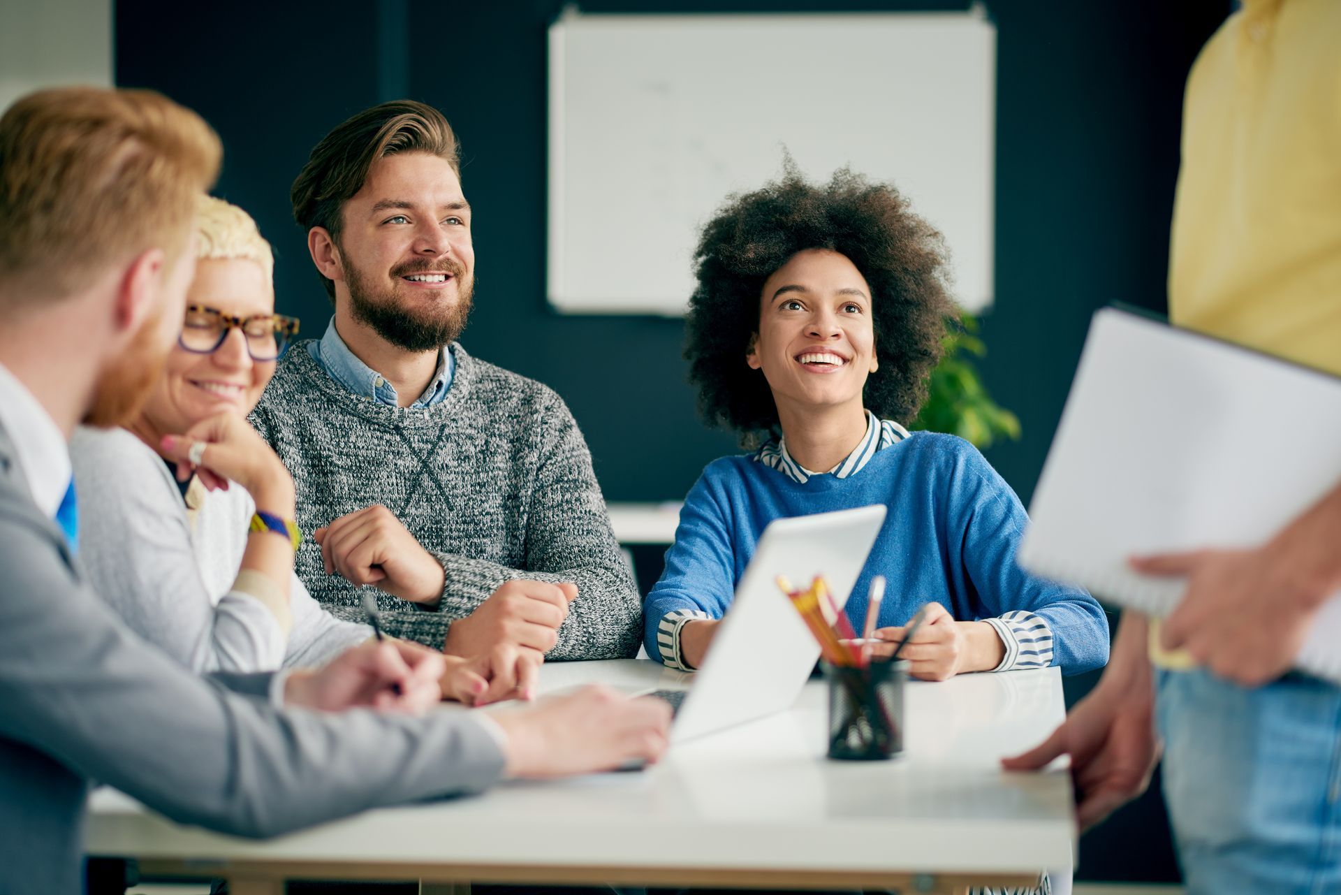 People smiling around a table in an office setting. A laptop is open. One person holds a folder.