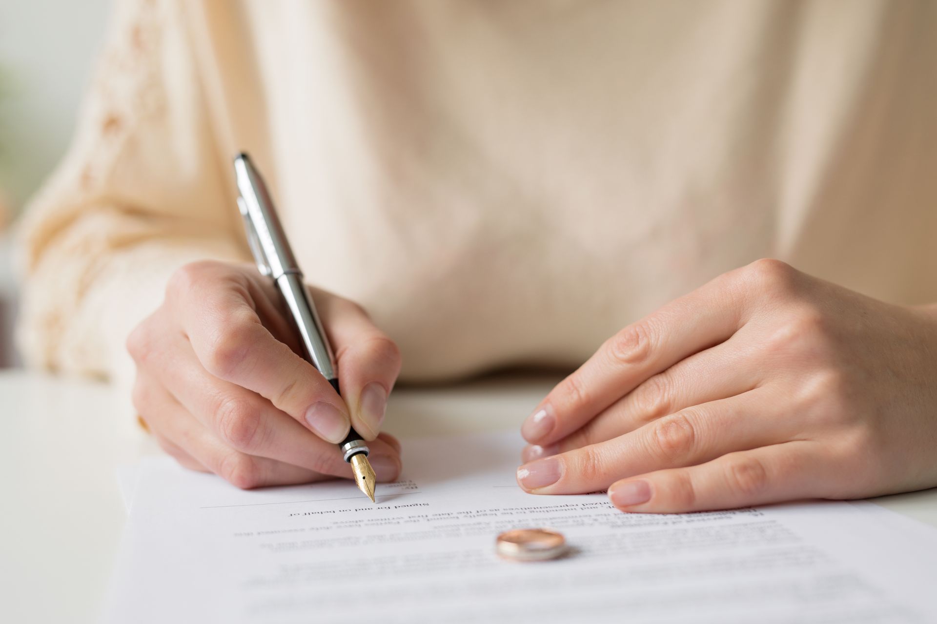 Person signing document, wedding ring on table.